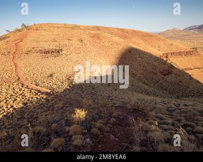 Mount Bruce (Punurrunha) summit shadow over the walking track along the  spinifex-clad western ridge. Karijini National Park, Western Australia Stock Photo