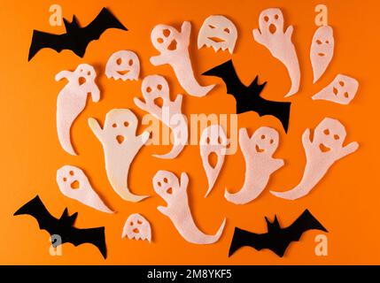 White ghosts and bat craft for Halloween party. Wrapping paper ghost on orange background top view. Cartoon creepy Whisper. DIY hand made. Set boo characters. Stock Photo