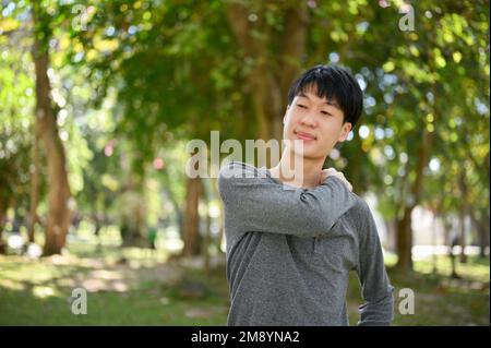 Handsome and happy young Asian man in casual clothes relaxing in the beautiful greenery park on the weekend. Stock Photo