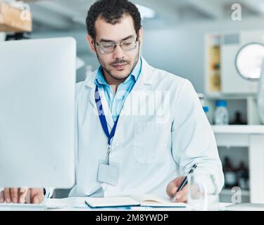 Deducing the facts. a young scientist writing notes while working on a computer in a lab. Stock Photo