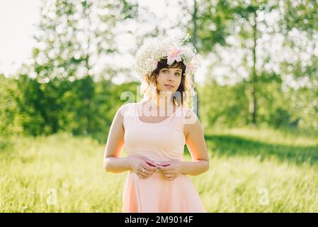 beautiful young girl with a wreath of flowers on her head smiling outdoors on a Sunny summer day Stock Photo