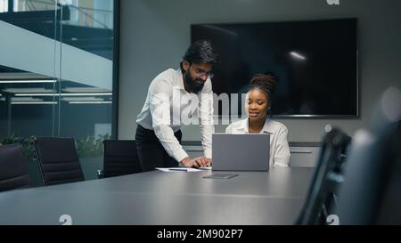 Male Indian Arabian bearded professional mentor businessman leader man helping African American female woman worker businesswoman teach intern explain Stock Photo