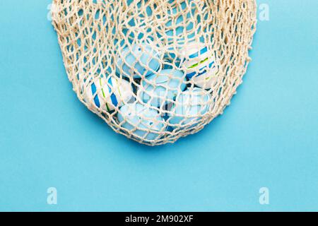 easter colorful painted eggs in the cotton string bag on blue background. Stock Photo
