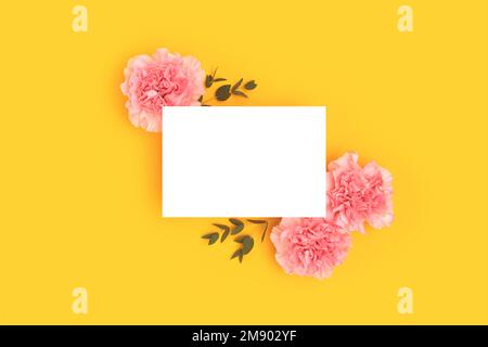 Empty paper card mock up, pink carnation flowers and green eucalyptus branches on a yellow background. Place for text. Stock Photo