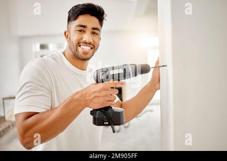 I like to design myself. a handsome young man standing alone in his home and using a power drill. Stock Photo