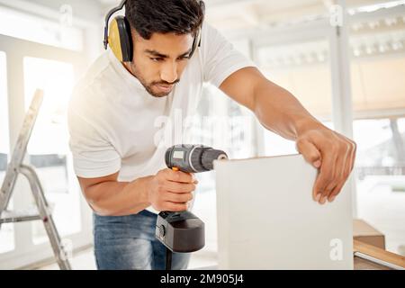 I know what Im doing. a handsome young man standing alone in his home and using a power drill. Stock Photo