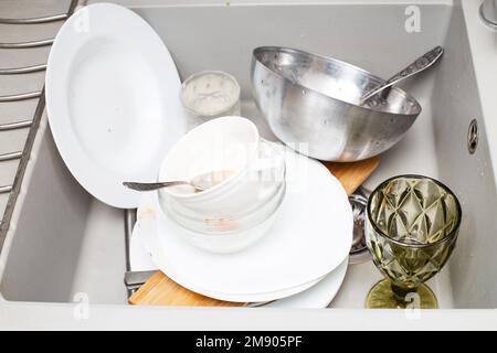 Pile of dirty dishes like plates, cutlery in the grey modern granite sink in the kitchen. Stock Photo