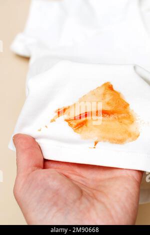womans hand hold white shirt clothes with ketchup stain on a beige background. Stock Photo