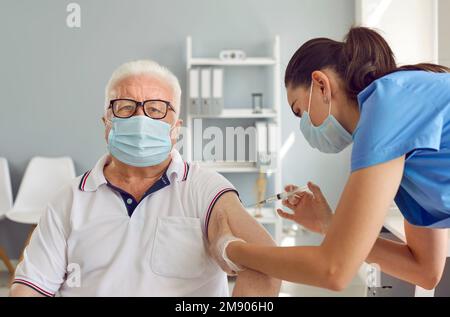 Senior man in medical protective mask receives vaccination against COVID-19 at vaccination center. Stock Photo