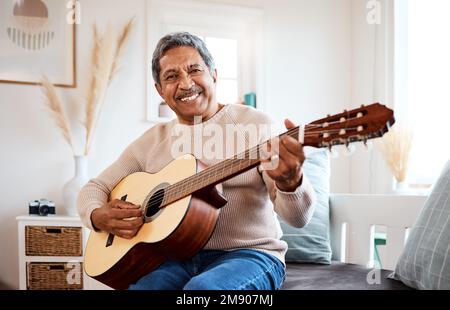 Hes been playing for years. a senior man playing the guitar at home. Stock Photo