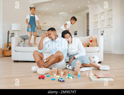 Can we get some rest. a young couple looking stressed at home while their kids play around them. Stock Photo