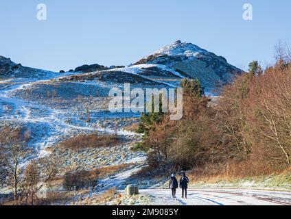 Holyrood Park, Edinburgh, Scotland, UK. 16th January 2023. Snow cover and icy roads and pavements in the Scottish capital, early morning temperature of minus 3 degrees centigrade. Pictured: A couple walk along the icy pavement with the summit of Arthur's Seat in background. Credit: ArchWhite/alamy live news. Stock Photo