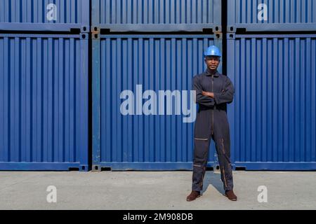 portrait of worker black african american man standing arm cross and working in freight cargo commercial shipping dock with container background. indu Stock Photo