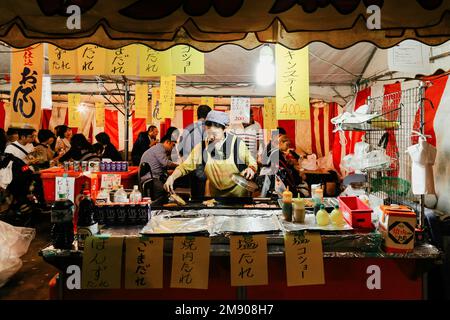 Tokyo, Japan - November 1, 2022 : Local Japanese street food at night market in Tokyo, Japan.  woman grilling yakitori pork and chicken at street food Stock Photo