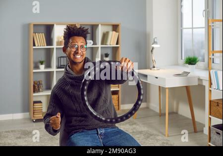 Young funny excited indian guy keeping steering wheel sitting on a chair at home. Stock Photo