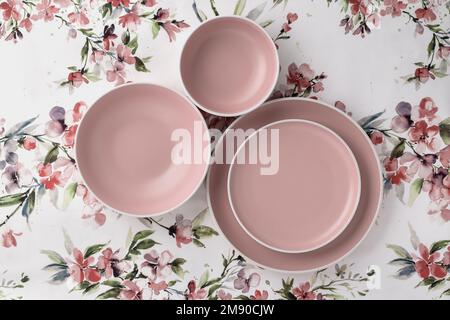Empty clean plates on a white tablecloth with floral pattern, table top view. Flat lay, minimalistic design. Pink ceramic crockery. Trendy tableware s Stock Photo