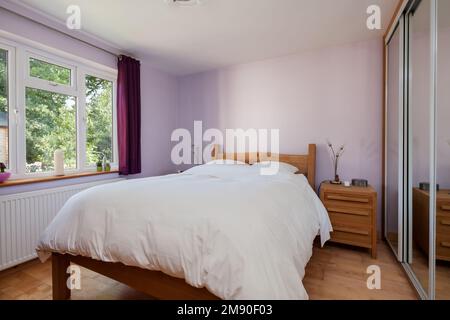 Furnished lilac bedroom with mirrored wardrobe and double bed Stock Photo