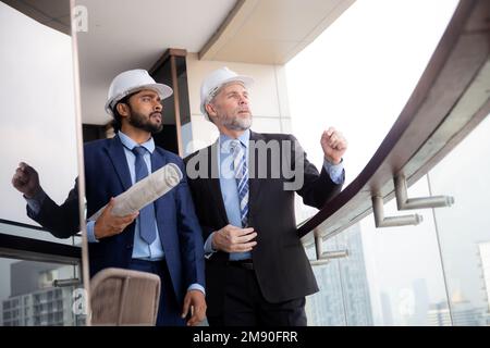 Senior architect inspector talking with contractor man together at office while holding blueprint building structure, executive and engineer planning Stock Photo