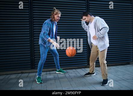 Man with down syndrome playing basketball outdoor with his friend. Concept of friendship and integration people with disability into society. Stock Photo