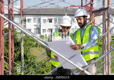 Two young architect discussion or contractor man while looking blueprint building structure together for survey on construction site, engineer plannin Stock Photo