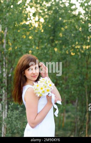beautiful young girl with a bouquet of daffodils in white dress outdoors in spring Stock Photo