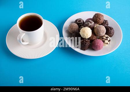 photo white cup with a drink and a plate with chocolates on a black background Stock Photo