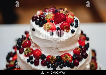 white cream wedding cake with fresh sweet strawberries, cherries, blueberries, black currants with three tiers close up Stock Photo