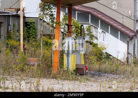 Old rusty gas station and dispensers abandoned and overgrown with vegetation on a sunny day. Summer. Stock Photo