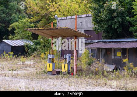 Old rusty gas station and dispensers abandoned and overgrown with vegetation on a sunny day. Summer. Stock Photo