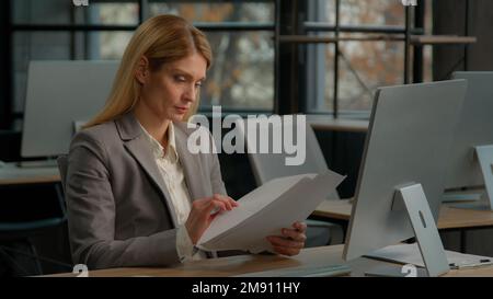 Caucasian middle-aged adult businesswoman executive manager entrepreneur boss bookkeeper woman office worker sitting at desk working with documents Stock Photo