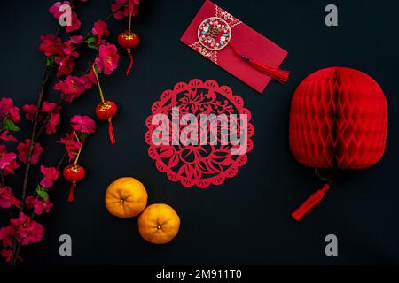 Chinese lunar new year decoration over red and black background. Flat lay concept with tangerine, red envelope, plum flower and festive decoration. Stock Photo