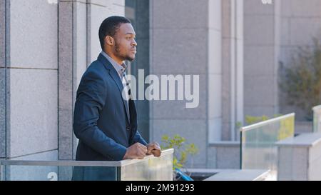 African American man pensive serious dreaming relaxed thoughtful employee taking break from work in office standing on balcony ethnic businessman male Stock Photo