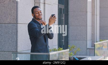 African American office worker standing on balcony speaking with colleagues with smartphone video chat app. Ethnic businessman entrepreneur manager Stock Photo