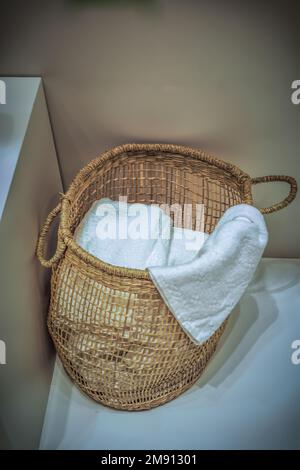 A wicker laundry basket full of fresh white towels on the floor Stock Photo