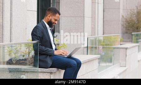 African American ethnic guy business worker freelancer man entrepreneur executive employer ethnic businessman working with laptop outdoors near Stock Photo