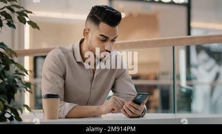 Indian Hispanic man typing smartphone scrolling social media male businessman online message reading news entrepreneur chatting browsing with Stock Photo