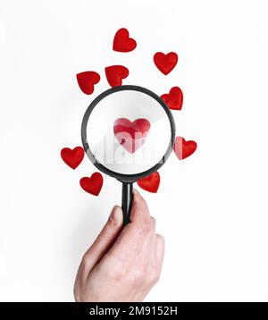 Magnifying glass increases one red heart among other hearts Stock Photo