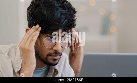 Close-up arab business man student male bearded boss leader with glasses guy works with laptop problems suffers from headache massages head feeling Stock Photo
