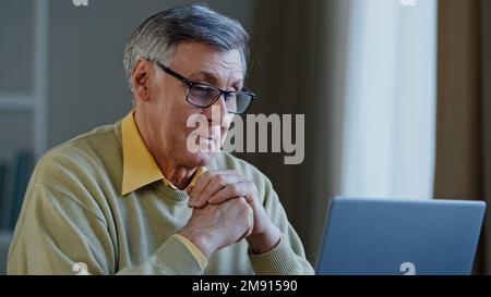 Old Caucasian man elderly mature senior businessman worker entrepreneur grandfather at office at home at table with laptop working thinking idea Stock Photo
