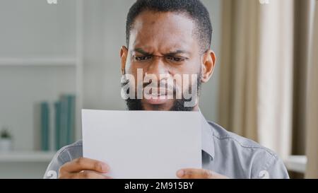 Unhappy African American bearded guy man received bad news reading letter with bank refuse feeling stressed about dismissal notice. Angry sad ethnic Stock Photo