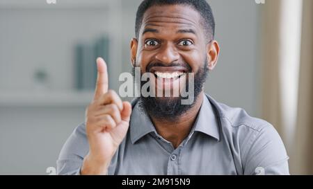 Happy exited bearded African American ethnic man entrepreneur businessman worker manager in office looking at camera rise forefinger index finger come Stock Photo