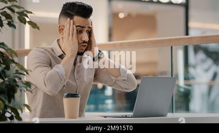 Sad shocked stressed Hispanic Indian man worker manager freelancer entrepreneur manager in cafe has problem with laptop app reading bad news worried Stock Photo