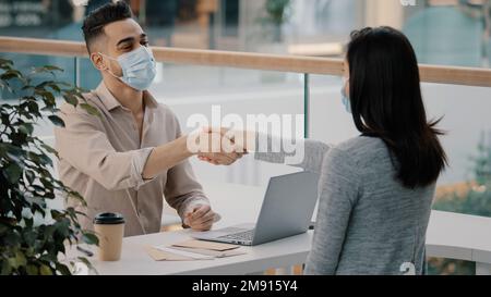 Man bank worker insurance agent man in medical mask advises consulting girl woman client about loan give cash money dollars credit shaking hands Stock Photo