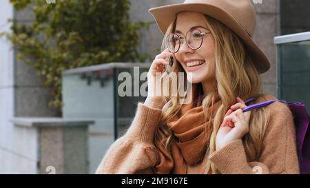 Portrait 20s girl answer phone call Caucasian female shopper buyer client on street in city holding shopping packages bags lady woman communicate Stock Photo