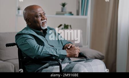 Pensive dreaming calm alone elderly patient. old African bald man with gray beard senior mature grandpa sit on wheelchair at home looking away dreams Stock Photo