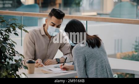 Bank worker in medical mask businessman salesman insurance man realtor manager talking with female client woman advises financial consultation with Stock Photo