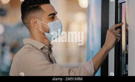 Side view male passenger Indian Hispanic man in medical mask in airport terminal businessman in bank office using self-service machine online payment Stock Photo