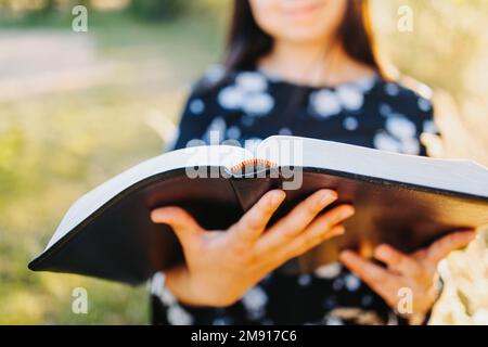 Unrecognizable religious girl holding and reading her bible, outside in the field at sunset. Selective focus Stock Photo