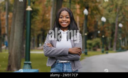 Ethnic 30s businesswoman looking at camera millennial African American girl smiling woman girl standing in park outdoors posing arms crossed portrait Stock Photo