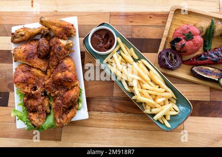 Baked chicken in adjika spices, baked vegetables and french fries, abkhasian style cuisine, on wooden table, Tbilisi, Georgia Stock Photo